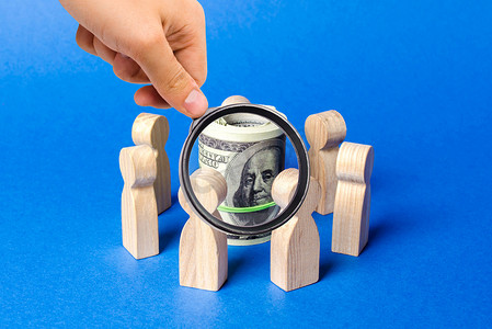 投资方案摄影照片_放大镜看着被人影包围的一捆美元。