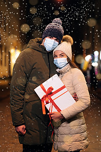 一对戴着医用防护面罩的夫妇在明亮的花环装饰中一起庆祝圣诞夜。