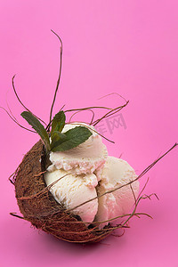 白色冰淇淋球摄影照片_粉红色背景中用薄荷叶装饰的空椰子中的香草冰淇淋球
