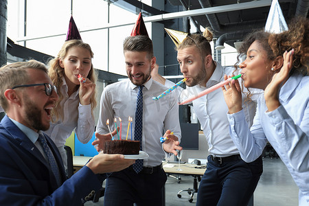 商业聚会摄影照片_快乐的商业团队带着生日蛋糕在办公室聚会上向同事致意