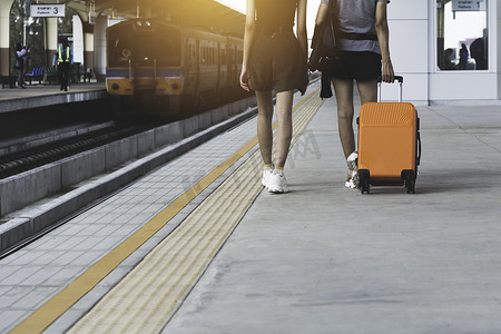 拖着橙色手提箱行李袋，走在火车站的女人