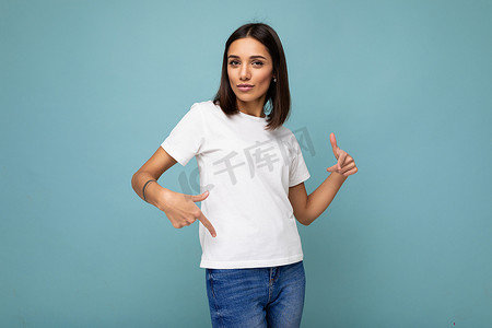 穿着休闲白色 T 恤、自信迷人的黑发年轻女性，在蓝色背景中与自由空间隔离开来做模型