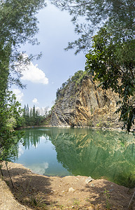 绿色矿山摄影照片_翠绿色的池塘 由开挖石灰岩矿山造成 蓝天白云 数以吨计的木头