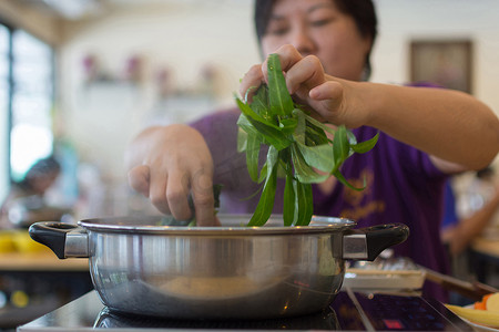 铃木里美摄影照片_亚洲妇女将蔬菜放入火锅中做饭
