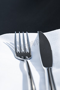 精美菜单摄影照片_户外豪华餐厅的桌上放着白色餐巾的叉子和刀子，婚礼或活动的精美菜单以及餐饮服务理念