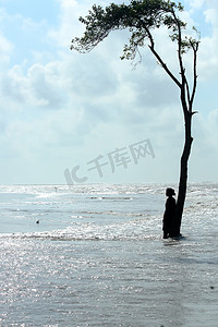 一位孤独的千禧年单身女性远远地站在蓝海海浪表面的一棵树下。