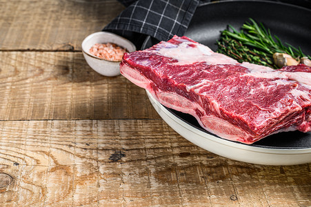 新鲜生牛肉短肋肉放在平底锅上，配上香草。