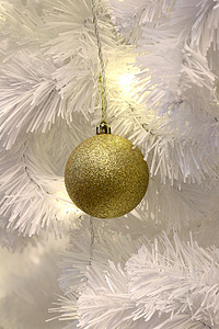 金球摄影照片_白色圣诞树背景装饰上的金球（选择性焦点）