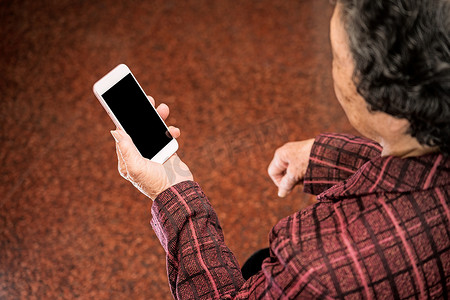 老人技术摄影照片_亚洲老妇人坐着看现代智能手机上的东西，与家里的其他人建立联系，生活技术，特写