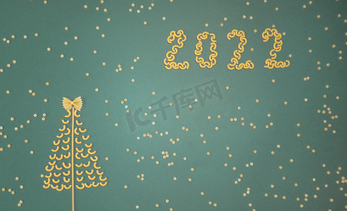 圣诞数树摄影照片_圣诞树上排列着干意大利面和数字 2022，以及绿色纸背景上的意大利面星星。
