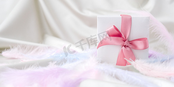 白色礼品盒，白色丝绸纹理背景上有粉红色丝带。