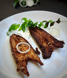印度餐厅风格的辣鱼苗放在白盘中，并用咖喱叶和洋葱镀得很漂亮