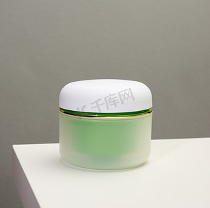 桌子上的罐子摄影照片_白色桌子上的化妆品的绿色罐子。