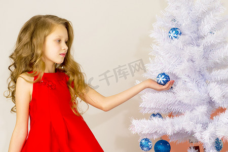 蓝色的物品摄影照片_摆在拿着蓝色中看不中用的物品的白色圣诞树旁边的女孩。