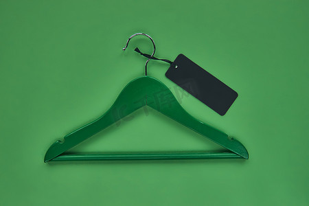 服装海报背景摄影照片_与黑纸标签隔离在绿纸背景上的木衣架。