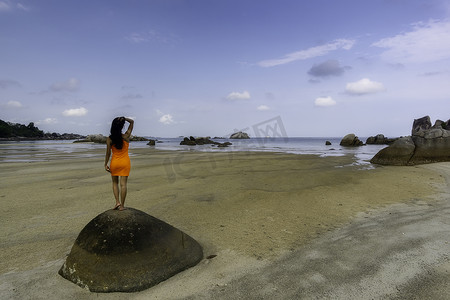 穿着橙色裙子站在大石头上的女人