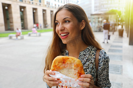 快乐的年轻女商人在她短暂的午休时间吃一个小披萨。