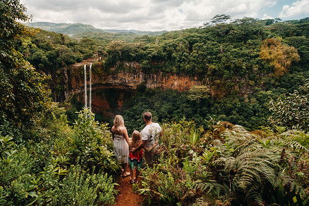 一个家庭，一个男人，一个女人和一个女儿，站在毛里求斯岛 Chamarel 公园瀑布附近的悬崖边上。一对夫妇和他们的女儿在毛里求斯岛的丛林中看着一个大瀑布落下