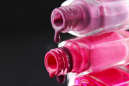 黑色深色背景中，带有复制空间的红色胡须粉红色指甲油从瓶子的瓶子里流出
