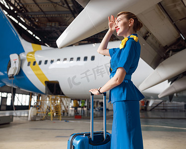 身着亮蓝色制服的漂亮空姐带着手提箱站在客机前，望向别处
