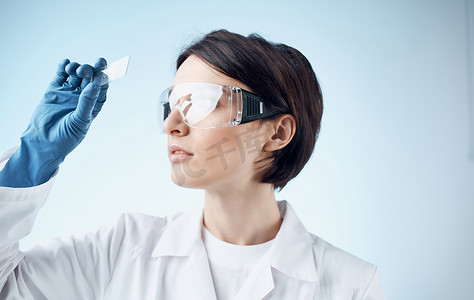 戴着医用手套的女实验室助理从显微镜下看玻璃