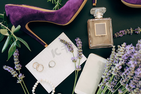 绿色背景中的淡紫色高跟鞋、一瓶香水、智能手机、珠宝和鲜花