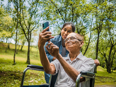 坐在轮椅上的祖父和孙女在公园里通过智能手机与亲戚进行视频通话。