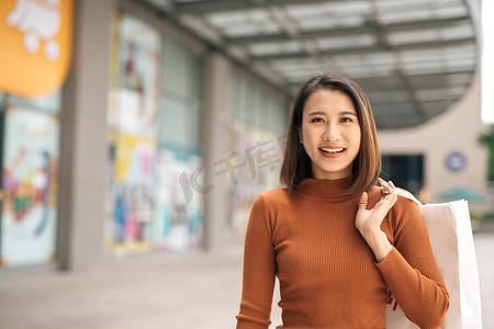 幸福、消费主义、销售和人的概念-在户外购物中心带着购物袋微笑的亚洲年轻女性