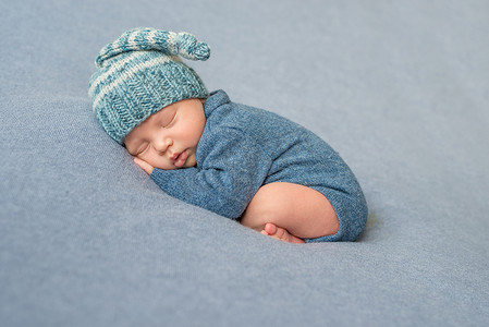可爱蓝色梦幻摄影照片_穿着蓝色连衣裤和帽子睡觉的新生儿