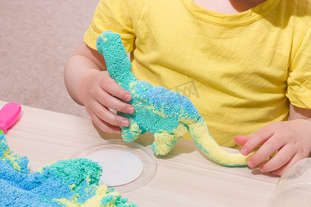 儿童小球摄影照片_孩子在桌上玩聚合物颗粒的橡皮泥，小球的原始橡皮泥，孩子玩橡皮泥的恐龙，在家里和孩子玩什么