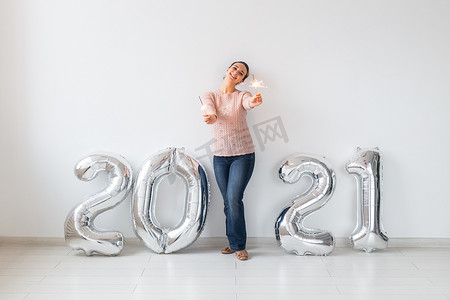 新年庆祝活动和派对理念 — 快乐的年轻女人，在白色背景的 2021 年银色气球附近放着火花。