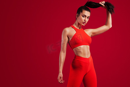 女性红色海报摄影照片_一位强壮的运动女舞者，穿着运动服、健身和运动动机，穿着红色背景，有复制空间。
