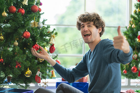 白人男子在装饰圣诞树时对着镜头竖起大拇指，开心地呆在家里庆祝。