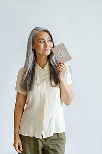 体贴的头发灰白的亚洲女顾客拿着站在浅灰色背景上的礼品卡