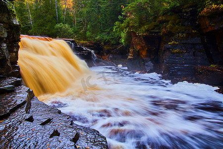 深绿的摄影照片_深绿森林中带金色和棕色巨型瀑布的湿石路