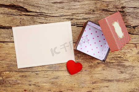 开盖摄影照片_带边框的空白粉色贺卡和带开盖的空红色礼品盒，木质背景上用红心装饰