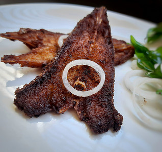 印度餐厅风格的辣鱼炸物放在白盘中，并用咖喱叶和洋葱装饰精美