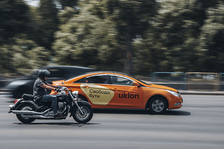 乌克兰，基辅 - 2021 年 6 月 27 日：橙色雪佛兰 Epica Uklon 出租车猫和铃木入侵者摩托车在街上行驶。