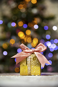 带粉色蝴蝶结的金色圣诞礼物，带圣诞树散景灯背景和复制空间，假日，呈现圣诞概念