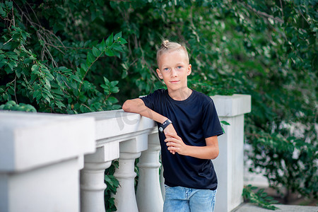 城市朋克摄影照片_穿着黑色 T 恤的时尚男孩少年在城市公园里。