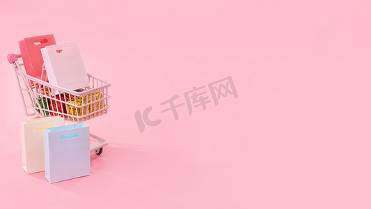 浅粉色背景摄影照片_年度销售购物季概念 — 迷你红色商店推车，里面装满纸袋礼物，浅粉色背景，空白复制空间，特写