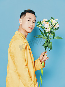鲜花的男人摄影照片_蓝色背景中穿着黄色外套、拿着一束鲜花的男人的侧视图