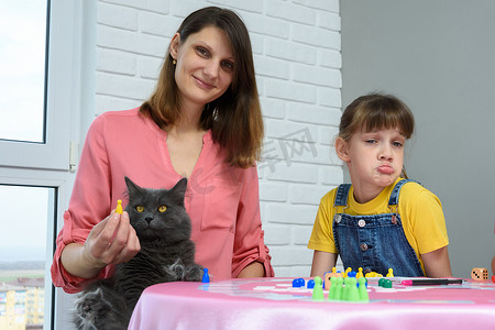 桌子上有一个快乐的女孩、一个不高兴的女孩和一只家猫