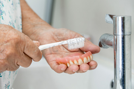 亚洲老年或老年老年妇女患者使用牙刷清洁替换牙齿的局部义齿。