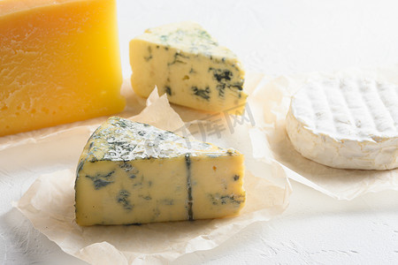 camembert摄影照片_奶酪拼盘：白色背景上的黄色 Maasdam、白色 Camembert 和蓝色奶酪 Dor Blue。