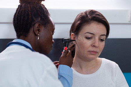 非洲裔美国耳科医生拿着医用耳镜分析生病的妇女病人的耳朵