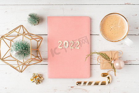 圣诞桌面摄影照片_顶部视图桌面圣诞粉红色记事本，带有 2022 个字母文本。