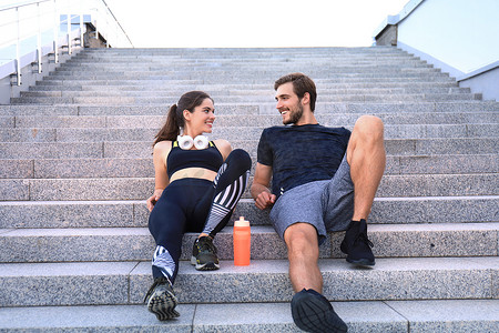在户外锻炼后，穿着运动服的年轻夫妇坐在楼梯上。
