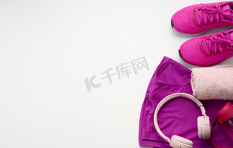 一双紫色纺织运动鞋、无线耳机、一条毛巾和一瓶白色背景的水。