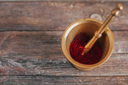 木质背景上的生有机红干藏红花香料，用带杵的老式金属黄铜砂浆